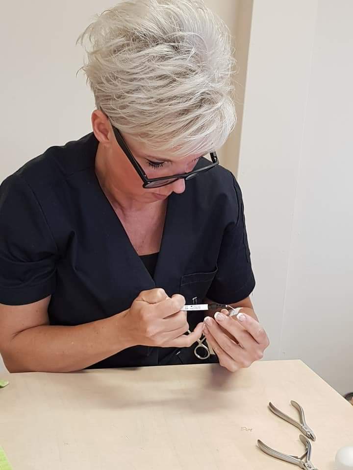 Monique werkt met precisie aan een nagel, met de tangen naast zich op tafel