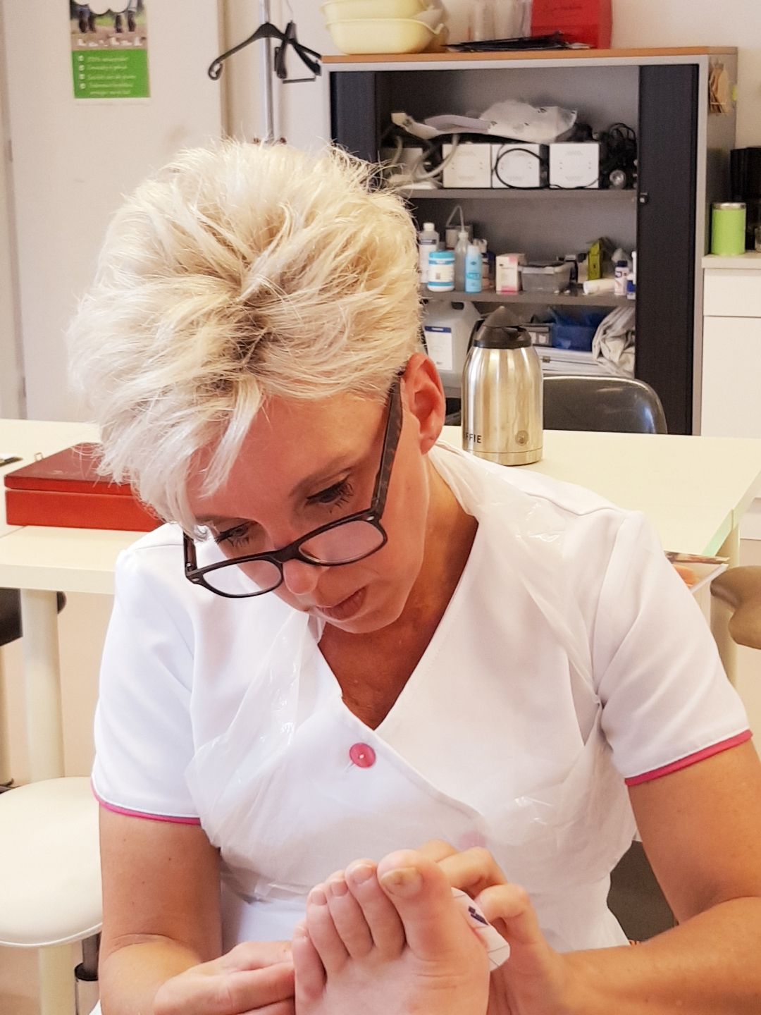Monique in haar witte tuniek, geconcentreerd aan het werk aan een voet